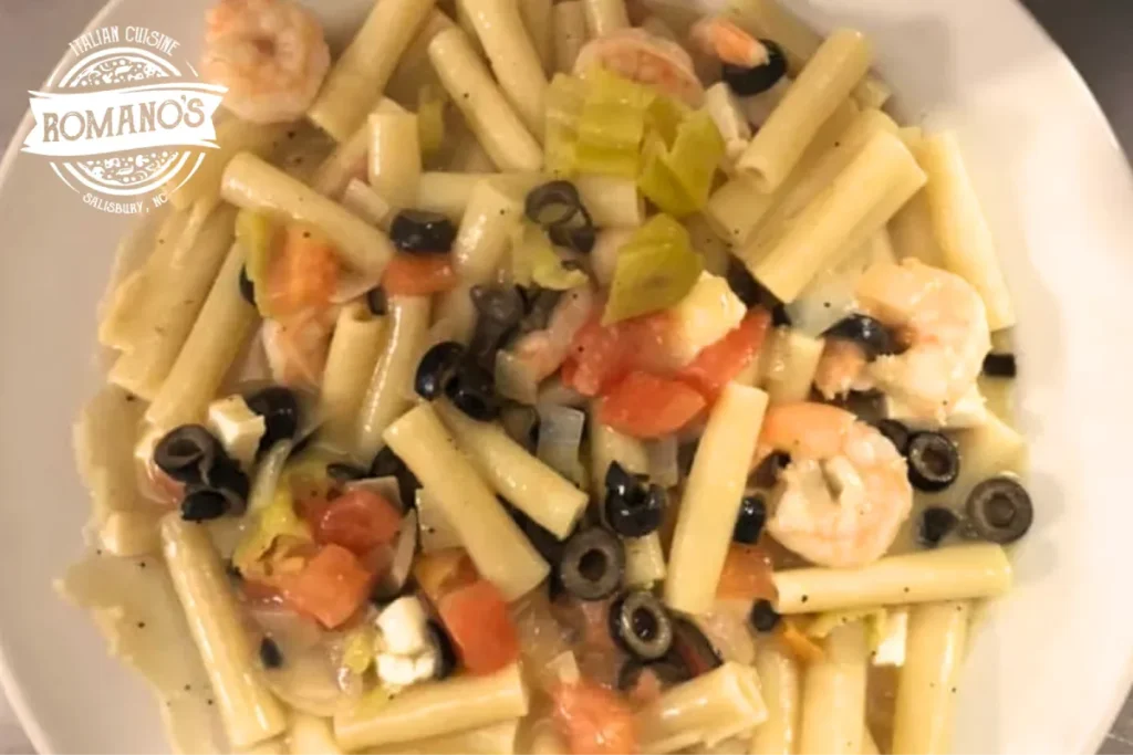 A close-up of pasta with shrimp, olives, tomatoes, and a creamy sauce.