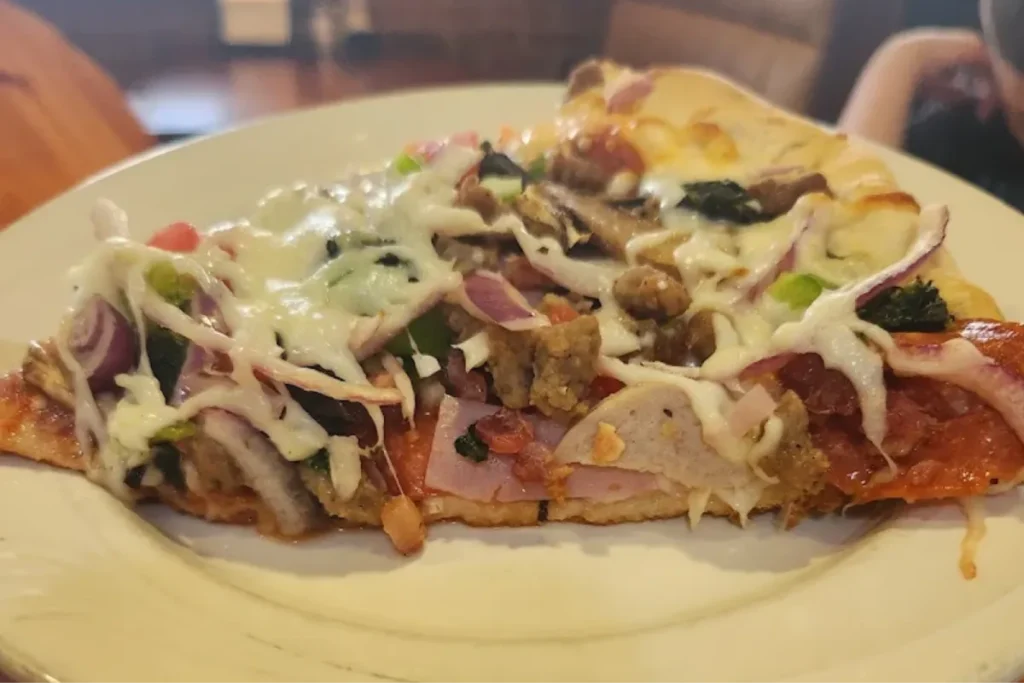 Loaded pizza slice with vegetables, meats, and melted cheese